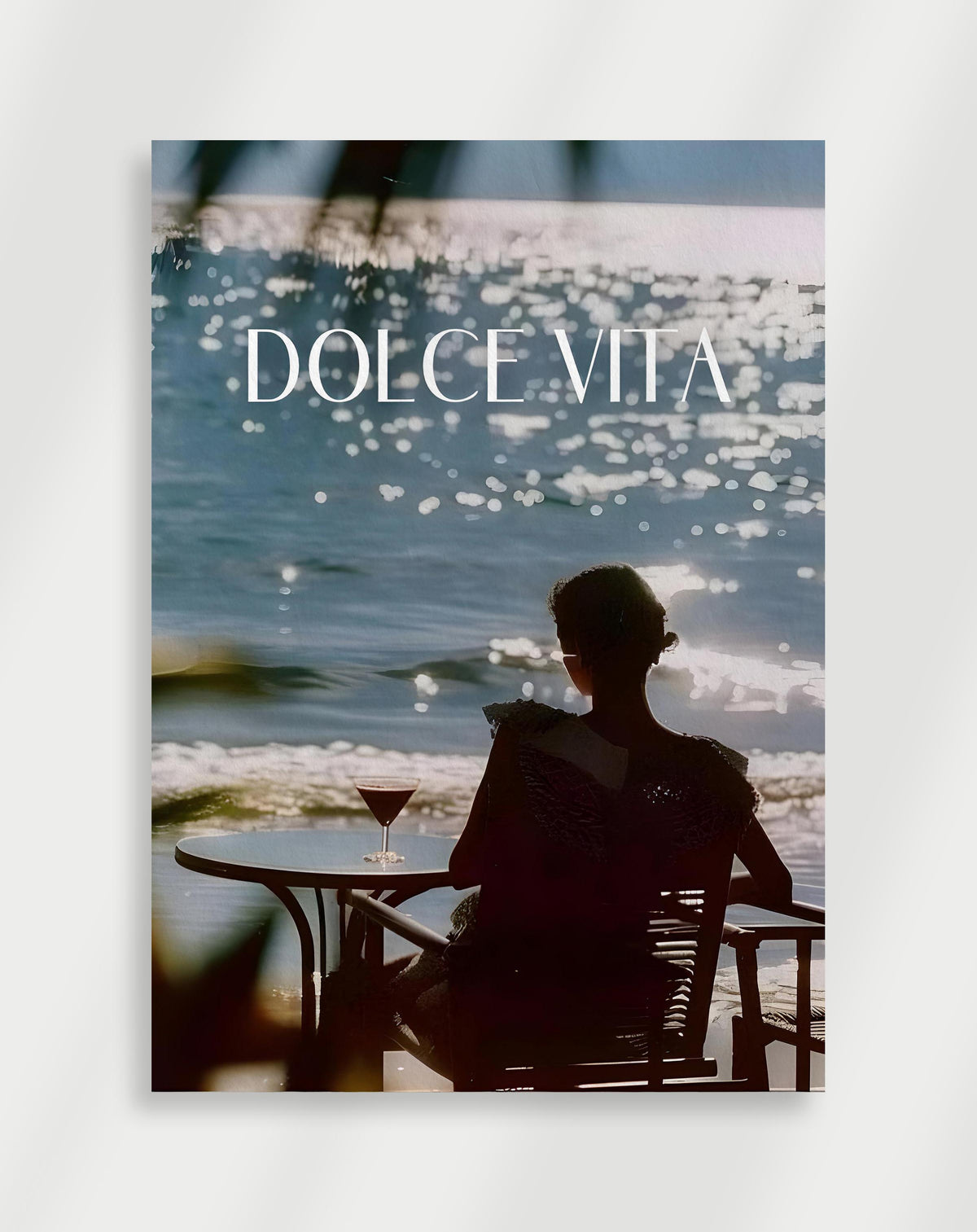 Woman by the sea poster with a woman sitting at a table by the sparkling sea with a cocktail and DOLCE VITA text
